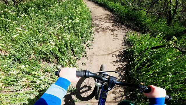 POV five year old boy rides bicycle on mountain biking path in summer