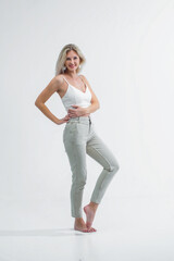 Fototapeta na wymiar A beautiful blonde with a sporty figure in light jeans and a white T-shirt poses in the studio on a white background