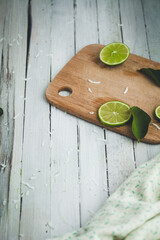Cut Limes and coconut shreds on cutting board on white washed table.