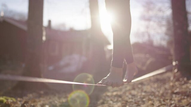 LENS FLARE SLO-MO - A female slack liners bare feet walking the strap