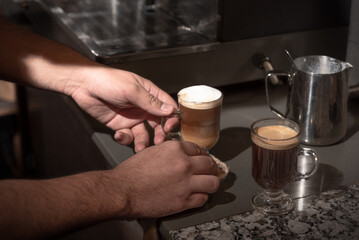 Manos de hombre, preparando dos cafés. Mesada de bar.