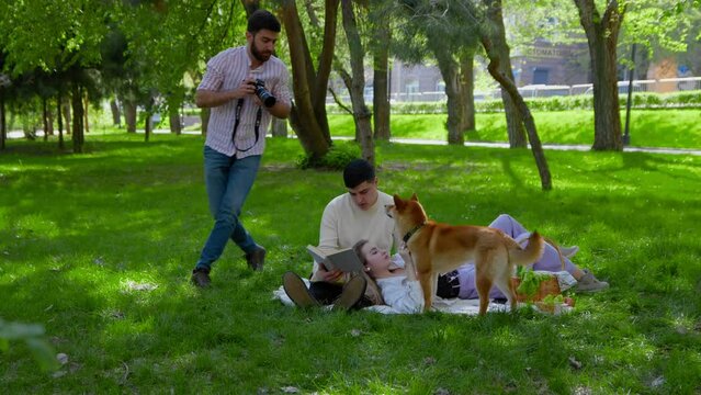 A photographer takes pictures with a camera of a young family with a dog on a picnic. Picnic in nature