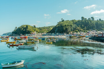 Colorful and wide horizontal shot of boats and lone boat at sunset in Caleta Tumbes with village and mountains in background, Chile
