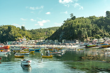 Wide colorful horizontal shot of boats and ships during sunset in Caleta Tumbes with village and mountains in the background, Chile