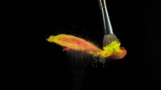 Makeup brushes touch each other on black dark background and small particles of color cosmetics, super slow motion, 1000 fps FullHd video