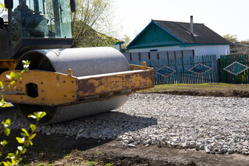 The roller rolls the gravel preparing the soil for the road. Rural road repairs in Kazakhstan.