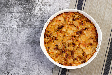 Oven baked potatoes with cheese, mushrooms and onions  in a white baking dish on a dark grey background. Top view, flat lay