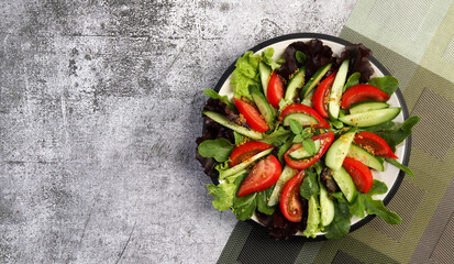 Summer cucumber Vegetarian salad with onions, tomatoes and lettuce on a round plate on a dark gray background. Top view, flat lay