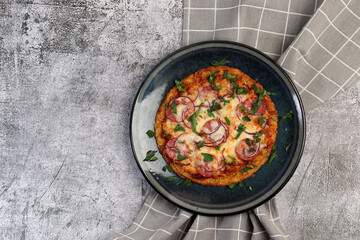 Grated Potato Crust Pizza with pink onions and salami on a round plate on a dark gray background. Top view, flat lay