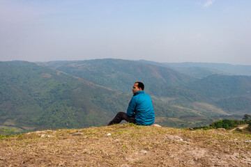 Fototapeta na wymiar man sitting alone at hill top with misty mountain rage background from flat angle