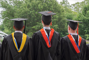View from behind of a group of three  students in graduation cap.