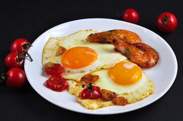 Fried eggs with shrimp in a frying pan. On a black background.