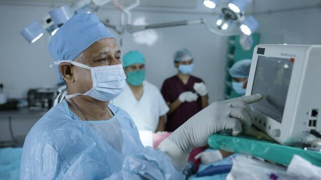 Surgeon in uniform using monitor for operation to patient at operation theatre - concept of technology, healthcare and treatment