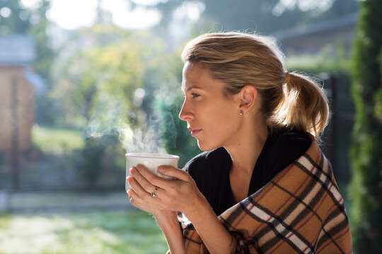 Pretty Blonde Woman Is Holding A Steaming Tea In Cup At Home In Garden, Morning Time.