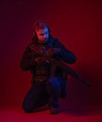 soldier in full gear with weapons. a man in headphones, body armor, with a backpack and a belt. red background. colored, blue-red light