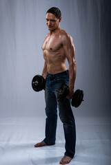 Sportsman posing, with dumbbells. Photo of an active man with a naked torso on a gray background. dynamic movement. Sports and healthy lifestyle