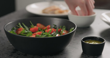 man hands put cherry tomatoes over fresh arugula in black bowl on concrete countertop