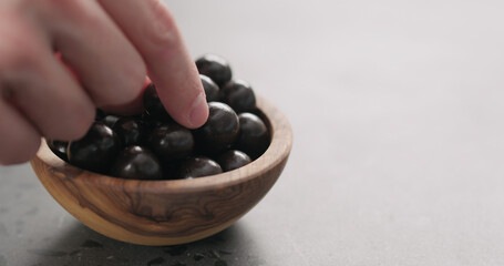 man hand take chocolate covered hazelnuts fall from olive wood bowl with copy space