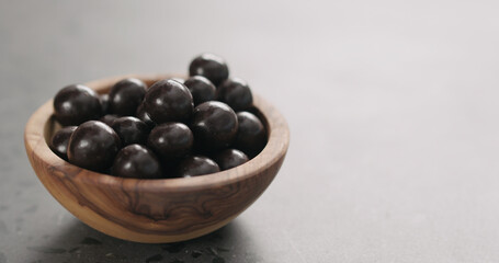 chocolate covered hazelnuts fall in olive wood bowl with copy space