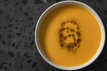 Pumpkin soup decorated with herbs and olive oil in white bowl on concrete background with copy space