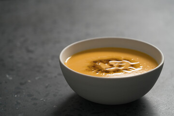 Pumpkin soup decorated with herbs and olive oil in white bowl on concrete background with copy space