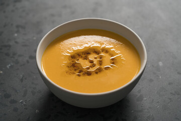 Pumpkin soup decorated with herbs and olive oil in white bowl on concrete background