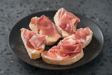 bruschetta with prosciutto and cream cheese on black plate on conctere background