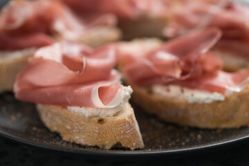bruschetta with prosciutto and cream cheese on black plate closeup