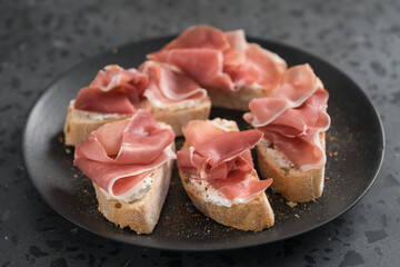 bruschetta with prosciutto and cream cheese on black plate on conctere background