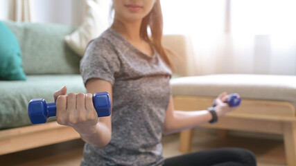 Fototapeta na wymiar Cropped shot young woman exercising with dumbbells in living room.