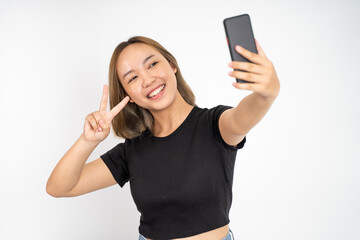 Naklejka premium attractive woman take a selfie using mobile phone camera with v sign finger gesture on isolated background