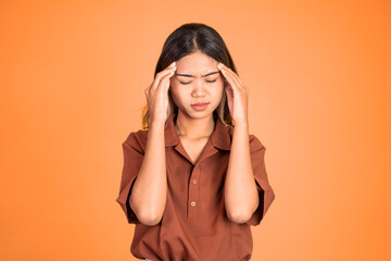 frustrated Asian young woman holding head with headache on isolated orange background