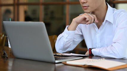 Obraz premium Focused young male employee analyzing financial data on computer laptop.