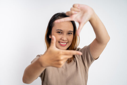 young woman looking at the camera from between fingers forming a frame on isolated background