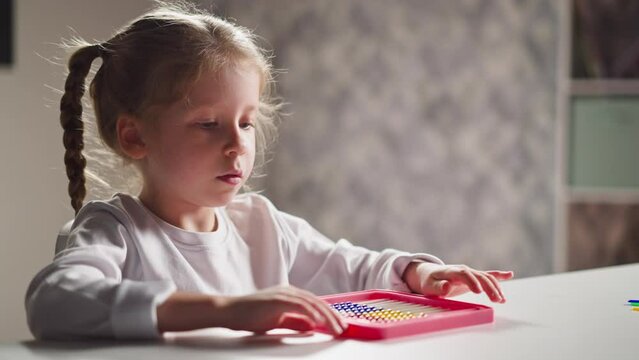 Thoughtful little girl student plays with colorful plastic abacus sitting at table during mental maths lesson in children room closeup slow motion
