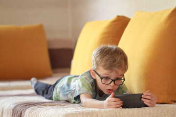 A boy of five years old, of European appearance, uses the phone.A boy of five years of European appearance lies on the sofa and talks on the phone.