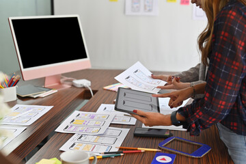 Thai Asian businesswomen work on adaptive media design by using digital devices and document papers with blank screen computer on wooden desk. Creative digital development concept.