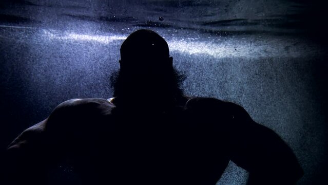 silhouette of a huge bald man in dark water. he's posing. close-up