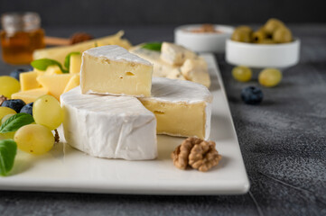 Cheese plate with a variety of cheeses, honey, grapes, nuts, olives, blueberries and fresh herbs on a concrete background. A festive snack.