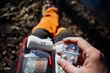 Pink pills, first aid kit, elastic bandage, the tourist takes a pill for nausea. the hand holds the...