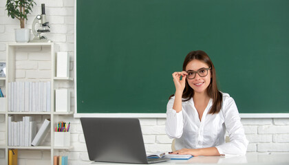 Female smilin college student in glasses working on a laptop in classroom, preparing for an exam.