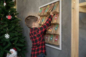 child boy taking a gift, handmade advent calendar day from craft bags with sweets. Eco friendly...