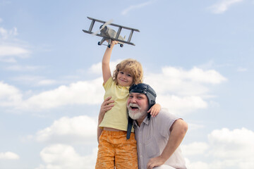 Young grandson and old grandfather playing with plane together on blue sky. Cute child with granddad playing outdoor. Weekend with granddad.