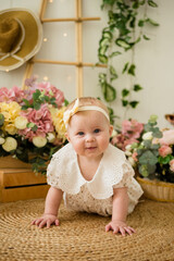 a smiling baby girl in a colored bodysuit with a headband crawls on the carpet among flower boxes