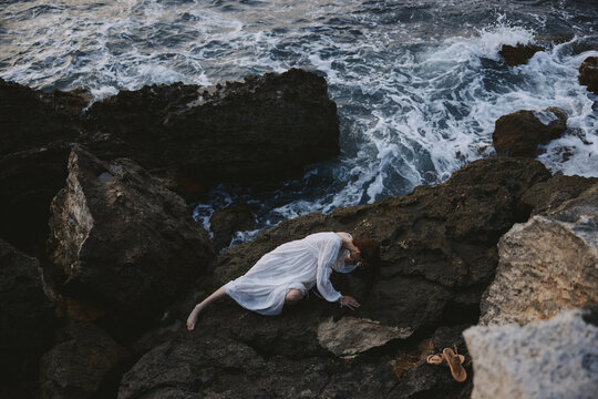 Beautiful bride in a secluded spot on a wild rocky coast in a white dress view from above