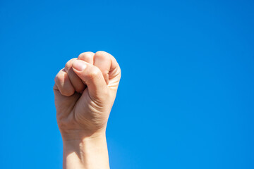 Clenched fist on sky background. Palm on a blue background