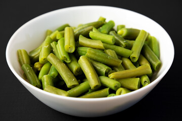 Steamed Green Beans in a White Bowl on a black background, side view. Close-up.