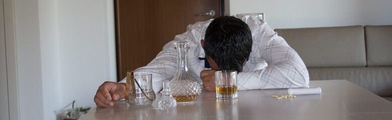 Image of a sleeping man leaning on the table at home after abusing alcohol, suffering from anxiety....
