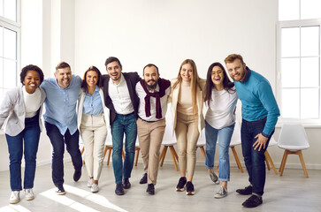 Team of young and successful multiracial people hug and smile at camera together. Portrait of happy smart and modern people in casual clothes standing in row, hugging and laughing. Team unity concept.