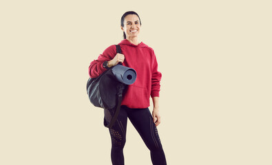 Studio shot of smiling female athlete in workout outfit with gym mat and sports bag. Happy...